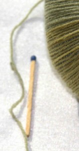 Nahaufnahme eines einzeln Fadens der zeigt wie filigran die Wolle ist; verdeutlicht durch ein daneben liegendes Streichholz